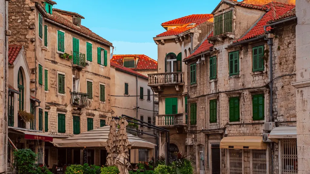 A quiet stone square in Split's old town at golden hour, with cafe umbrellas, green shutters and terracotta roofs above
