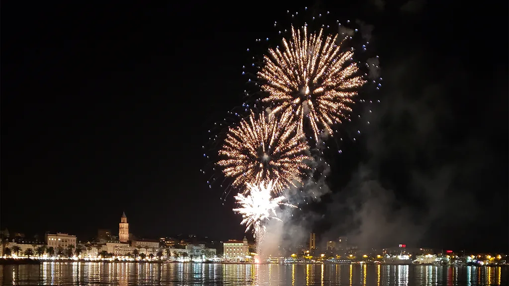 Fireworks over the Split waterfront at night, with the Riva lit up and the cathedral bell tower behind