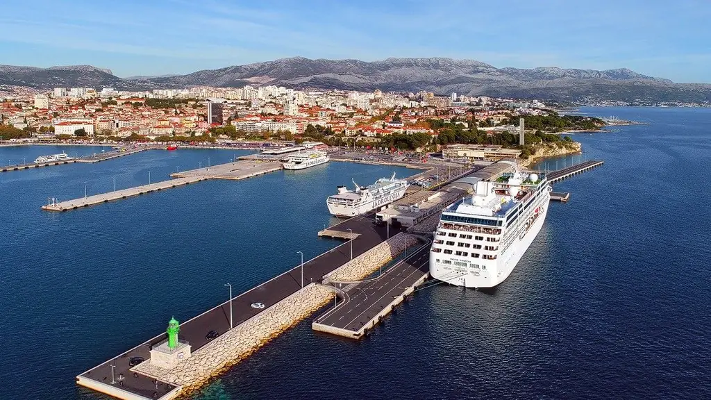 An aerial view of Split's passenger port with a cruise ship berthed alongside, island ferries behind it and the city and mountains beyond