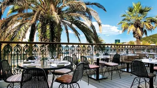 An empty café terrace with a wrought iron railing and tall palm trees in Split on a sunny day