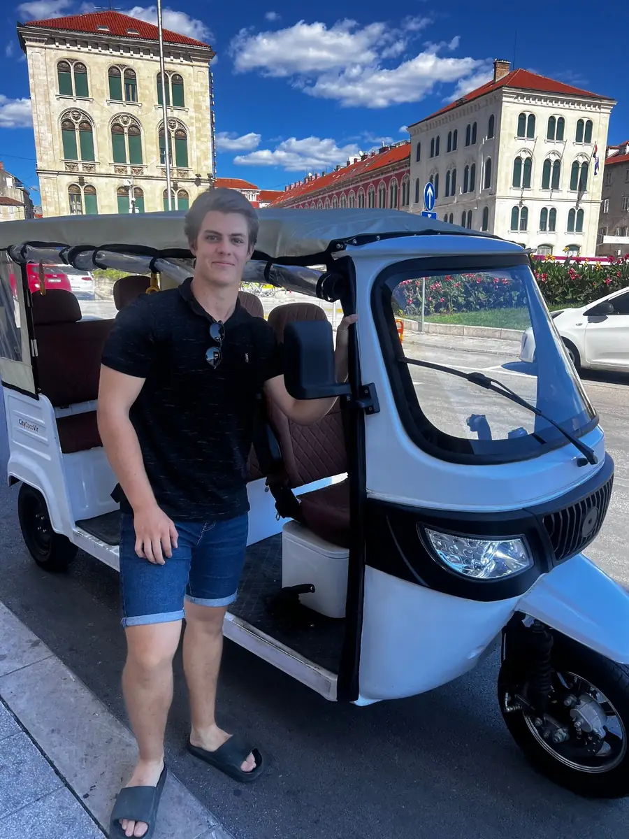 A guest leaning on a tuk tuk in front of Split's historic buildings